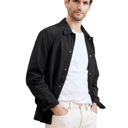 A man is wearing a casual black jacket with a collared shirt underneath, paired with cream-colored pants.
