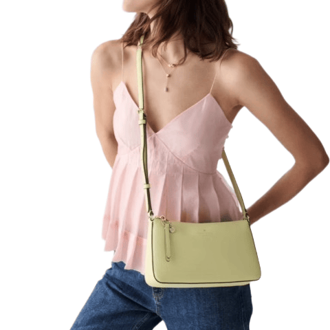 A woman wearing a light pink sleeveless top and blue jeans is carrying a light yellow crossbody bag.