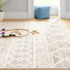 A cream and gray geometric pattern rug is on a wooden floor, with a small wooden train set and a blue cushion nearby.