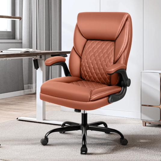 A brown leather office chair with quilted stitching, armrests, and a swivel base on casters, positioned next to a modern desk in a well-lit room.