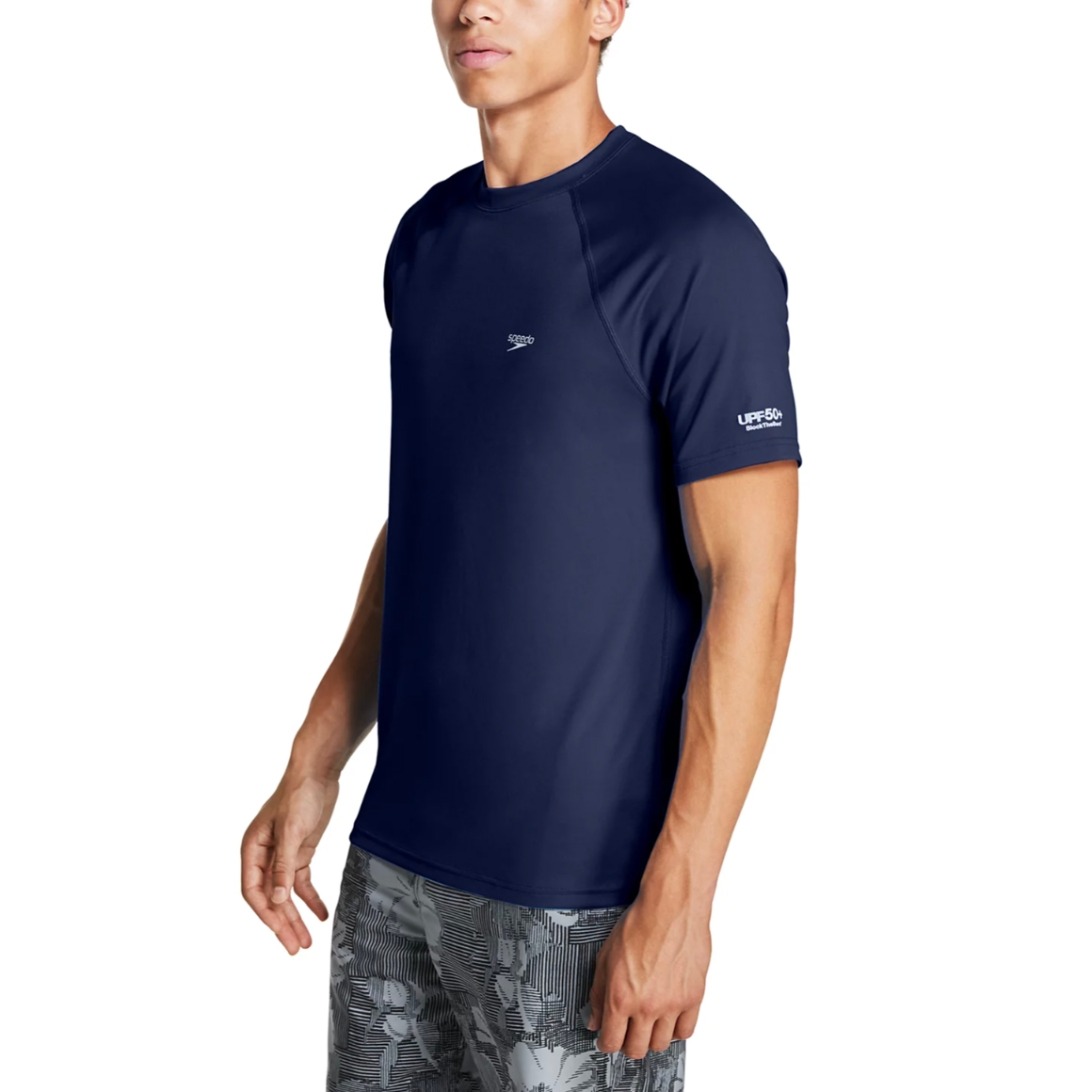 A navy blue Speedo rash guard featuring a small logo on the chest and \“UPF 50+\“ on the sleeve, designed for sun protection. Paired with gray patterned swim shorts.