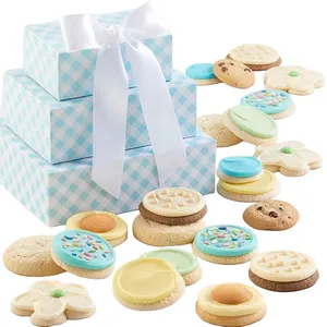 A stack of blue gingham-patterned gift boxes with a white ribbon is surrounded by assorted cookies, including decorated ones with icing and sprinkles, and flower-shaped cookies.