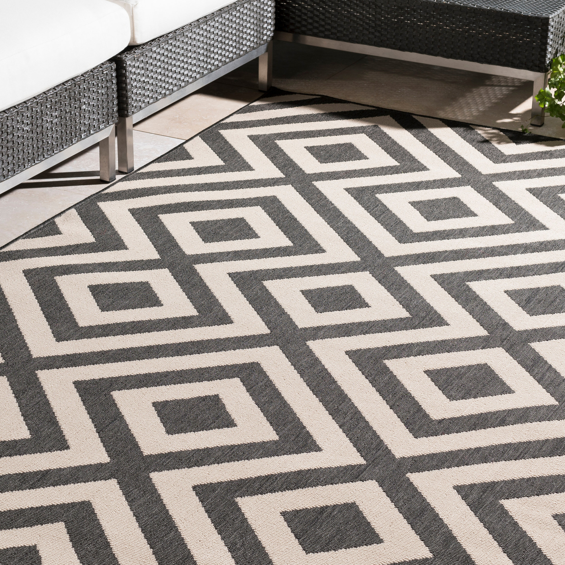 8' x 11' outdoor rug with a black and white geometric pattern featuring interconnected squares, placed near modern wicker furniture.