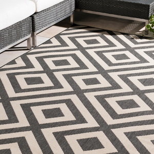 8' x 11' outdoor rug with a black and white geometric pattern featuring interconnected squares, placed near modern wicker furniture.