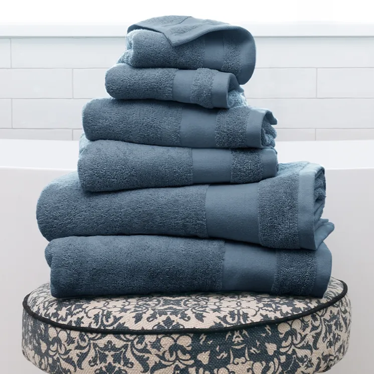 Stack of blue towels on a patterned stool with wooden legs, set in a bright, tiled bathroom.