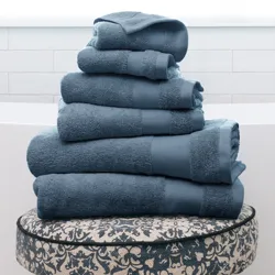 Stack of blue towels on a patterned stool with wooden legs, set in a bright, tiled bathroom.