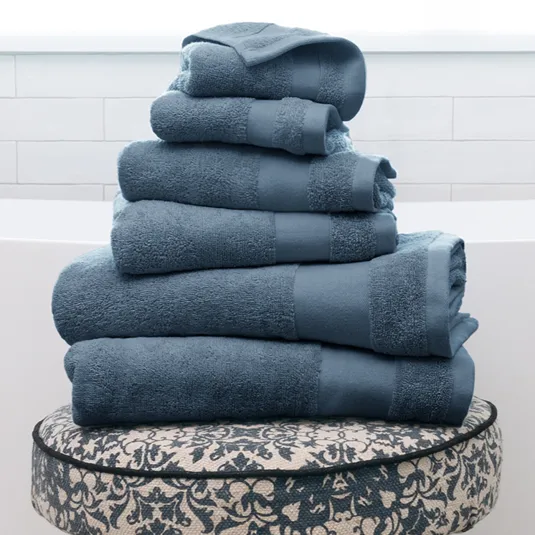 Stack of blue towels on a patterned stool with wooden legs, set in a bright, tiled bathroom.