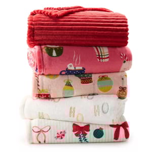 A stack of holiday-themed fleece blankets with festive patterns, including red ribbed, hot cocoa, holiday ornaments, and bows.