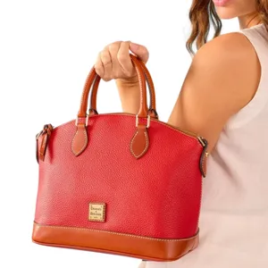 A woman holds a red leather handbag with brown trim and handles, featuring a gold label that reads \“Dooney & Bourke.\“