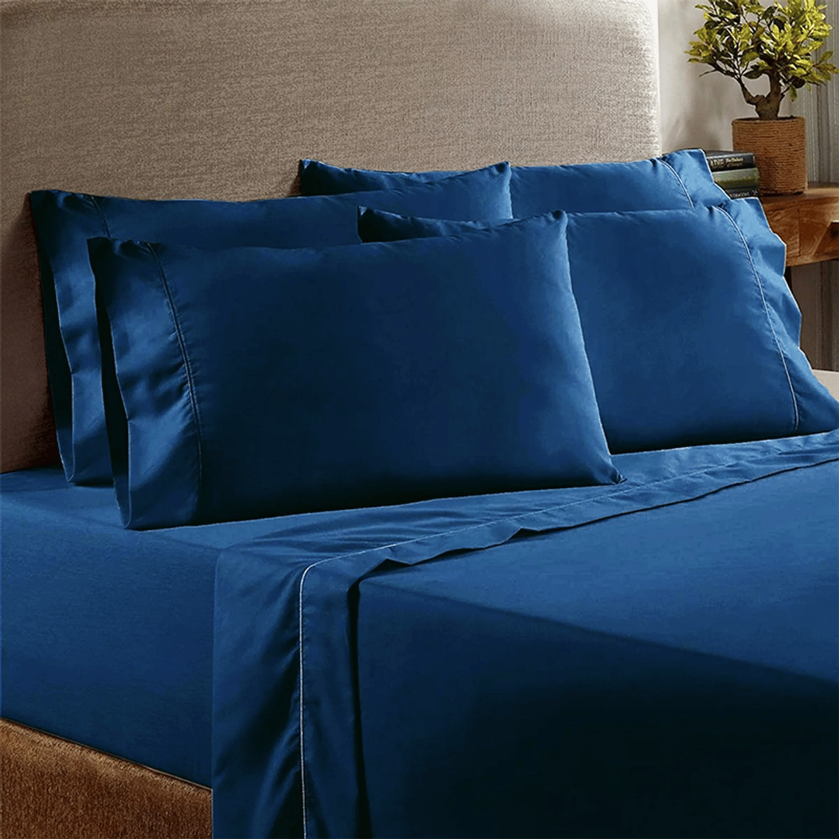 Blue bedsheet set with two large pillowcases on a bed, complemented by a wooden side table with a small plant.