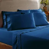 Blue bedsheet set with two large pillowcases on a bed, complemented by a wooden side table with a small plant.