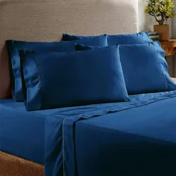 Blue bedsheet set with two large pillowcases on a bed, complemented by a wooden side table with a small plant.