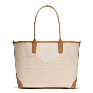 A stylish cream tote bag with tan leather accents, featuring the \“lululemon\“ logo embossed on the front.