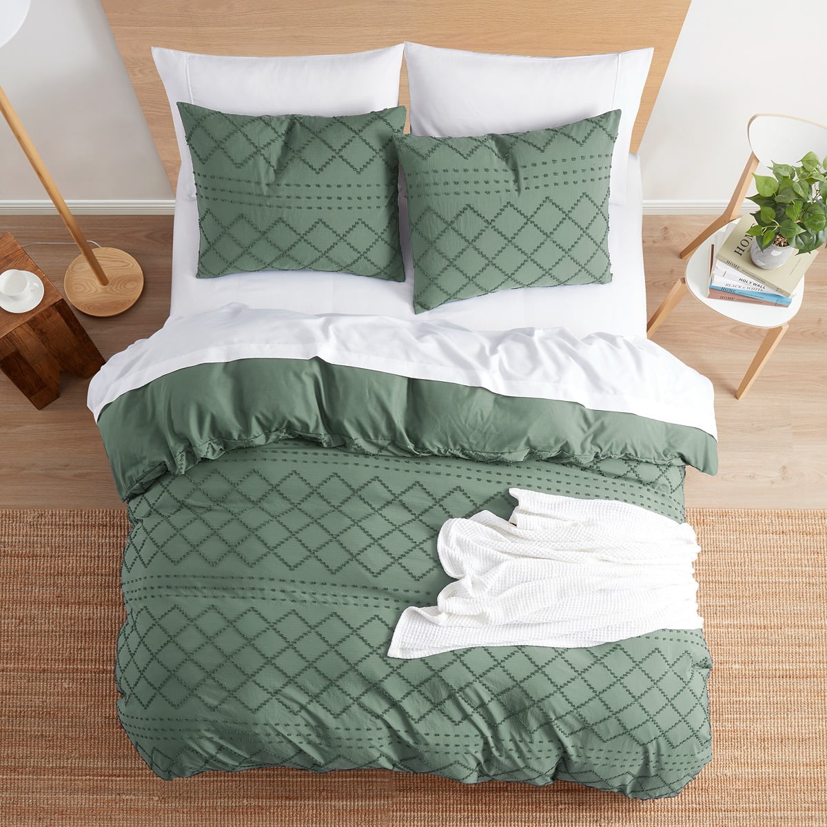 A neatly arranged bedroom set with green patterned bedding, including pillows, a duvet cover, and a white throw blanket.