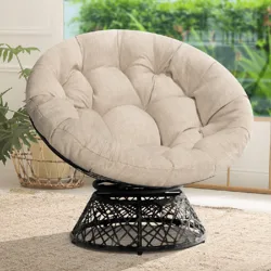 Cream-colored cushioned papasan chair with a woven black rattan base, placed in a cozy indoor setting with plants and a natural fiber rug.