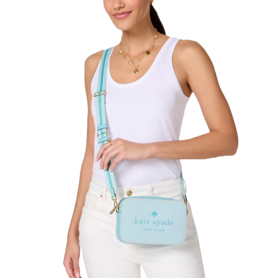 A woman wears a light blue Kate Spade New York crossbody bag with gold accents, paired with a white tank top and pants.