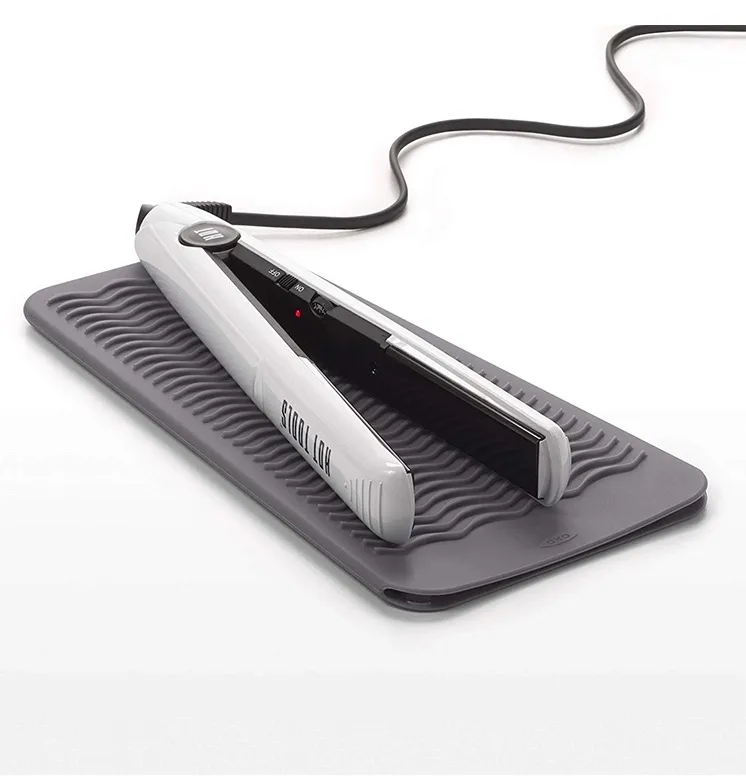 Two heat-resistant silicone mats designed to protect surfaces from hot curling irons, with one iron resting on top.