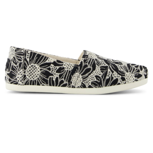 A black and white slip-on shoe with a floral lace pattern and a white rubber sole.