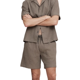 A man is wearing a textured short-sleeve button-up shirt and shorts set in a muted brown color.