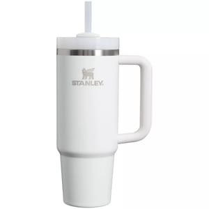 The Stanley Tumbler is a 30oz insulated travel mug with a handle and straw, designed in white with a stainless steel rim. It features the Stanley logo and is made for keeping beverages hot or cold.