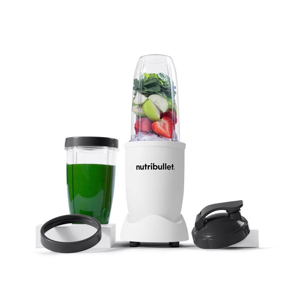 A NutriBullet blender set with a main blending cup containing fruits and vegetables, a separate cup with a lid filled with a green smoothie, a sealing lid, and a flip-top to-go lid.