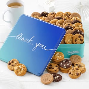 Mrs. Fields Nibblers Cookie Tin contains an assortment of small cookies like chocolate chip and white chocolate macadamia, presented in a blue tin with \“thank you\“ on the lid.