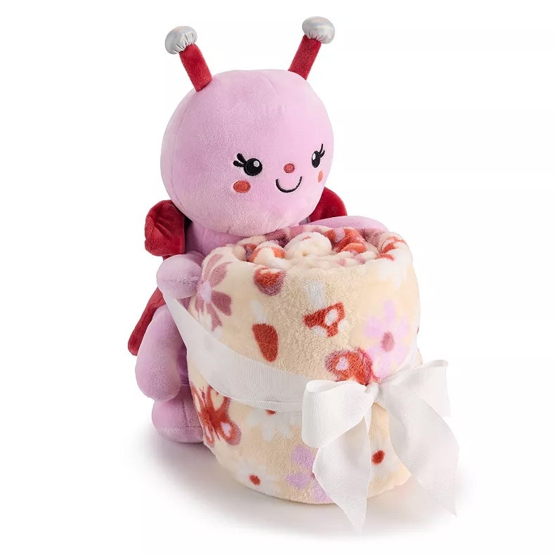 A pink plush ladybug holding a rolled-up floral-patterned blanket tied with a white ribbon.