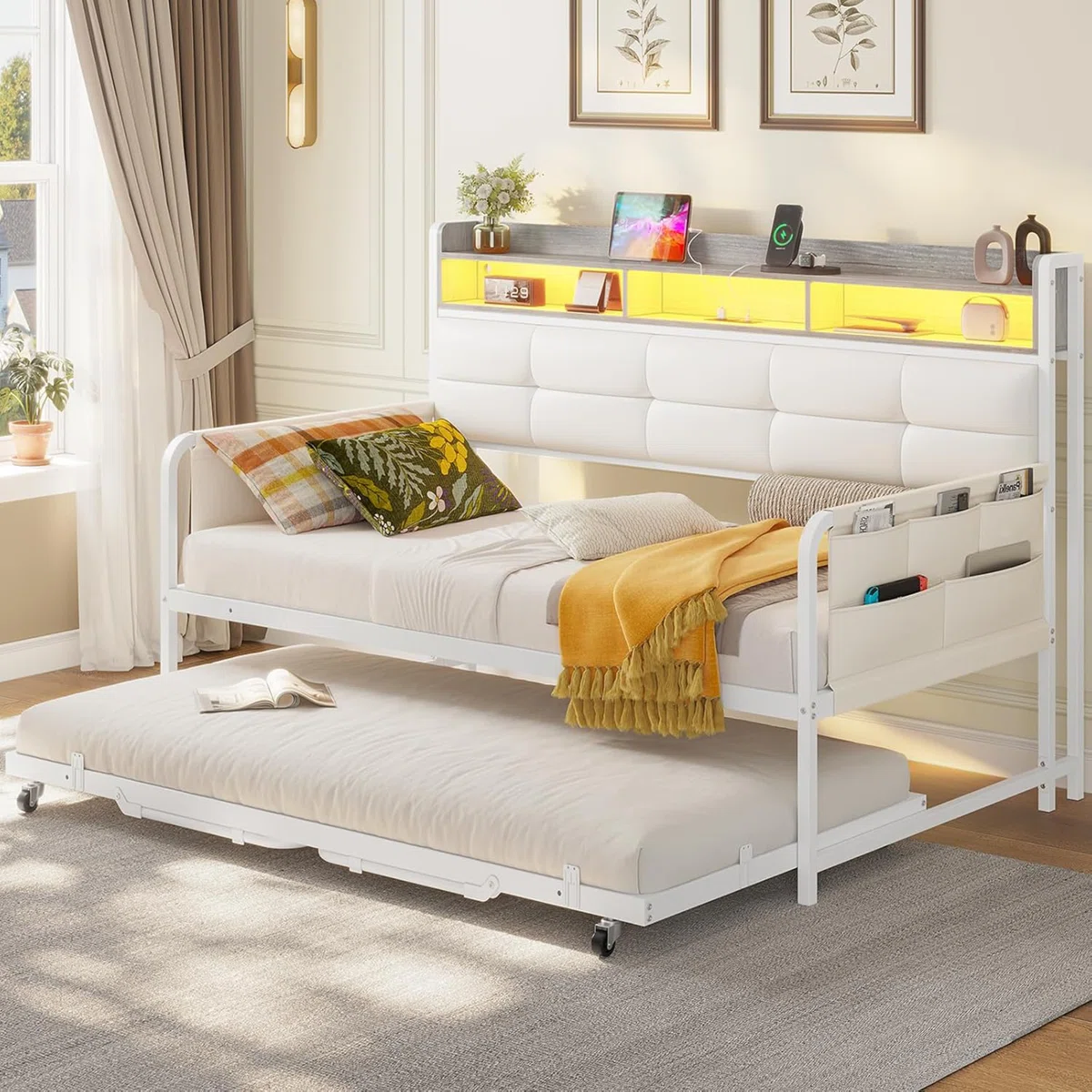 Daybed with trundle featuring a soft white upholstered backrest, built-in shelf with yellow lighting, and storage pockets on the side.