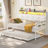 Daybed with trundle featuring a soft white upholstered backrest, built-in shelf with yellow lighting, and storage pockets on the side.