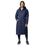 A person is wearing a long, navy blue, hooded puffer coat with dark leggings and hiking shoes.