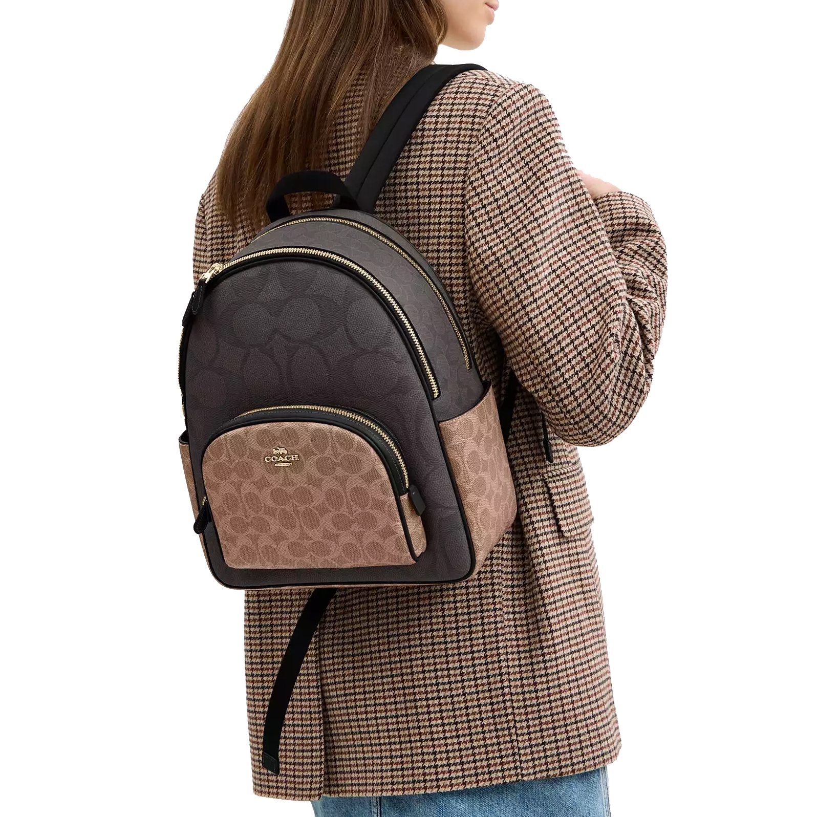 A person is wearing a Coach backpack with a signature pattern in black and brown, paired with a checked blazer and jeans.