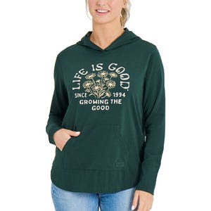 A green hooded sweatshirt features the phrase \“Life is Good Since 1994 Growing the Good\“ with a floral design on the front, paired with blue jeans.