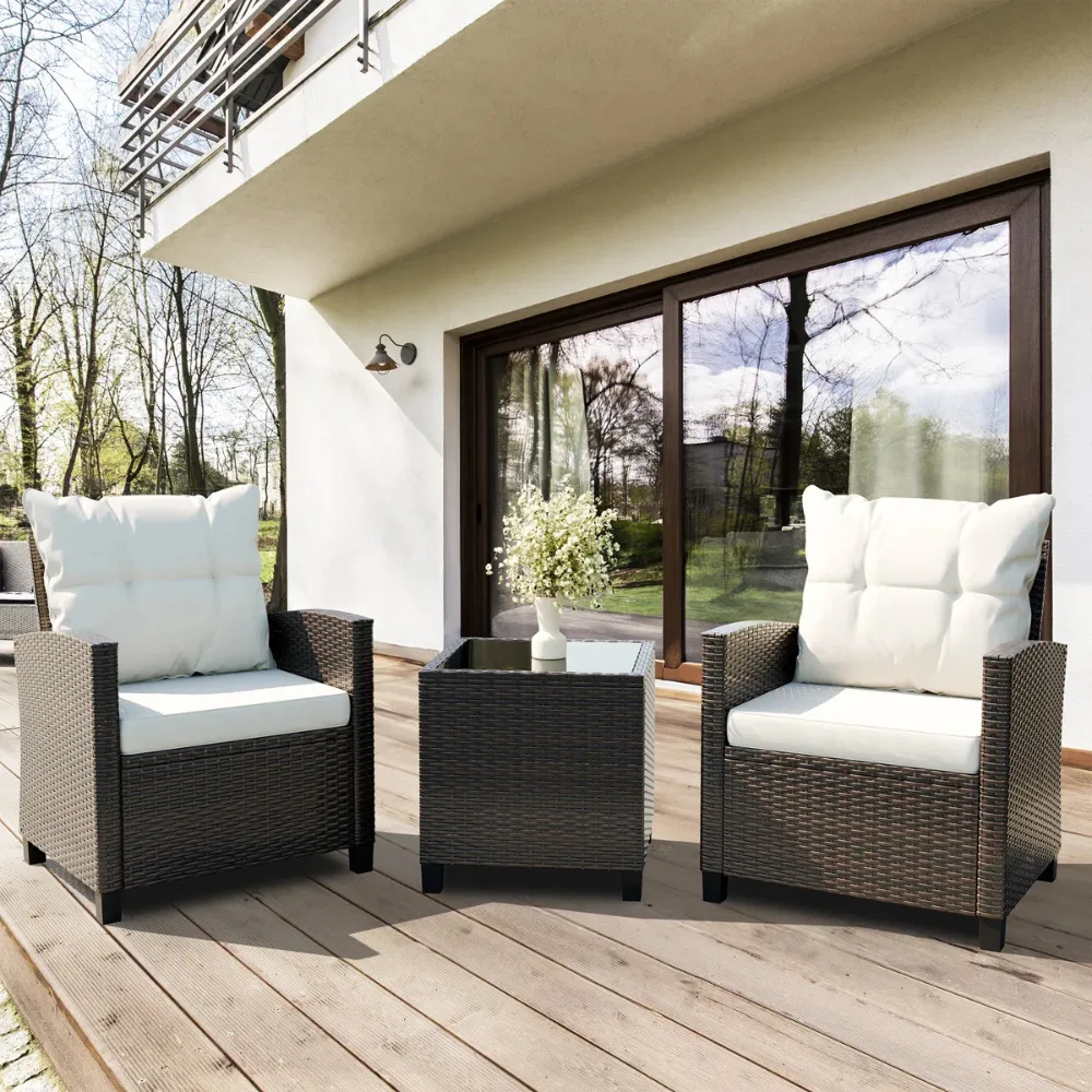 Outdoor patio set featuring two wicker chairs with white cushions and a matching wicker side table topped with glass, set on a wooden deck.