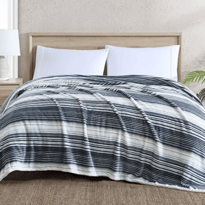 A striped comforter with varying shades of blue on a bed with white pillows and a wooden headboard.