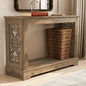 A wooden console table features intricate side cutouts, a flat top with books, a glass bottle, a lamp, and a wicker basket on the lower shelf.