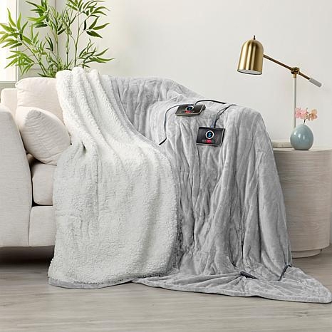 A gray heated throw blanket with a plush white sherpa lining is draped over a couch, featuring a visible control unit.
