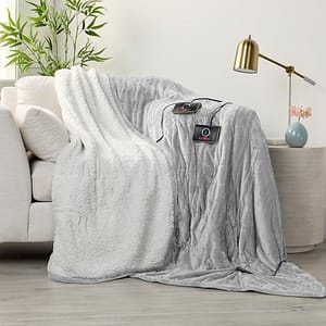 A gray heated throw blanket with a plush white sherpa lining is draped over a couch, featuring a visible control unit.