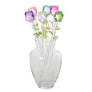A clear vase holds six colorful crystal roses with green stems and leaves.