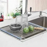 A roll-up dish rack with steel rods and a gray silicone edge rests over a kitchen sink, holding dishes and fruit.