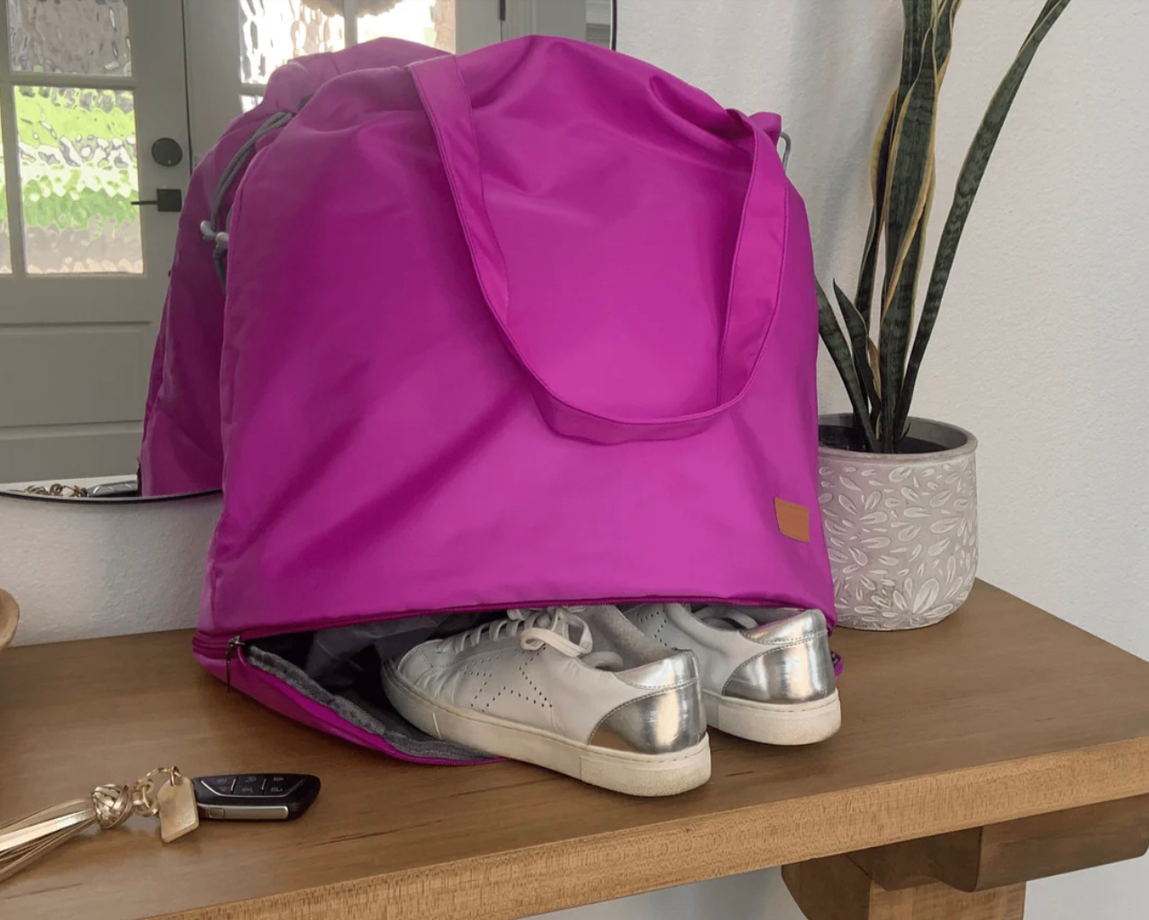 A vibrant pink nylon tote bag is perched on a table, with a special compartment underneath that's partially unzipped revealing a pair of silver-colored shoes.