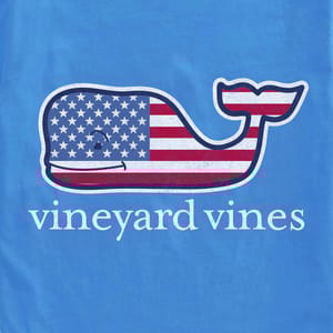 Blue tee featuring a smiling whale logo with an American flag design, accompanied by the text \“vineyard vines\“ below the whale.