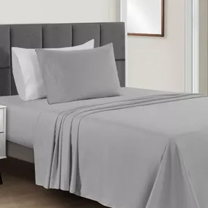 A neatly made bed with gray sheets and pillowcases, featuring a tufted gray headboard and white walls, alongside a small white bedside table.