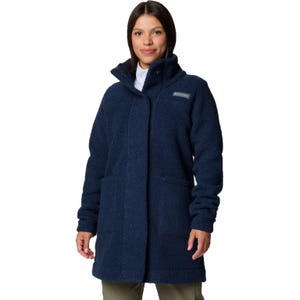 A woman wears a navy blue Columbia Long Sherpa Fleece, featuring a high collar, two front pockets, and a relaxed fit, providing warmth and comfort.