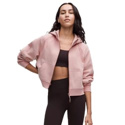 A woman is wearing a cropped, light pink hoodie paired with a black sports bra and high-waisted black leggings.