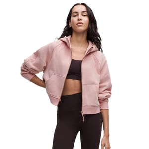 A woman is wearing a cropped, light pink hoodie paired with a black sports bra and high-waisted black leggings.