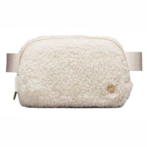 Lululemon fleece belt bag in cream features a soft, textured fabric with a zippered closure and adjustable strap. It has a small gold logo detail on one side.