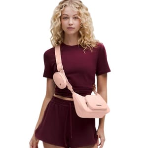 A woman in a burgundy outfit wears a peach-colored crossbody bag with a matching attached accessory holder.