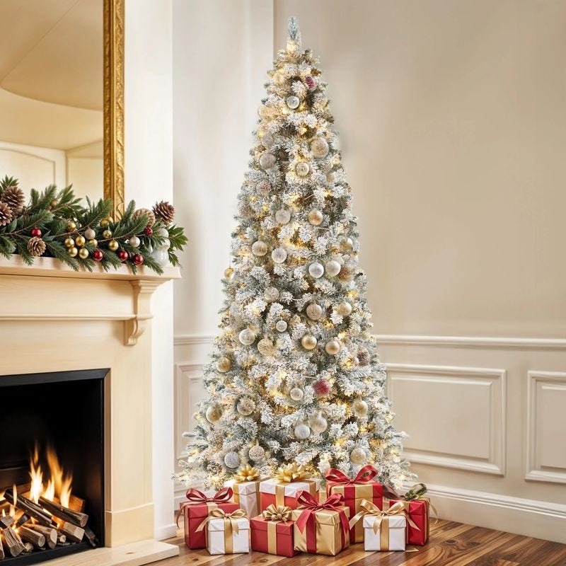 A white Christmas tree with gold and silver ornaments and lights, placed beside a fireplace decorated with garland. Several wrapped gifts in red and gold are arranged beneath the tree.