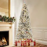 A white Christmas tree with gold and silver ornaments and lights, placed beside a fireplace decorated with garland. Several wrapped gifts in red and gold are arranged beneath the tree.