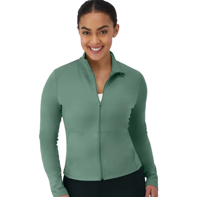 A smiling person is wearing a sage green zip-up jacket with long sleeves and a high neck, paired with black pants.